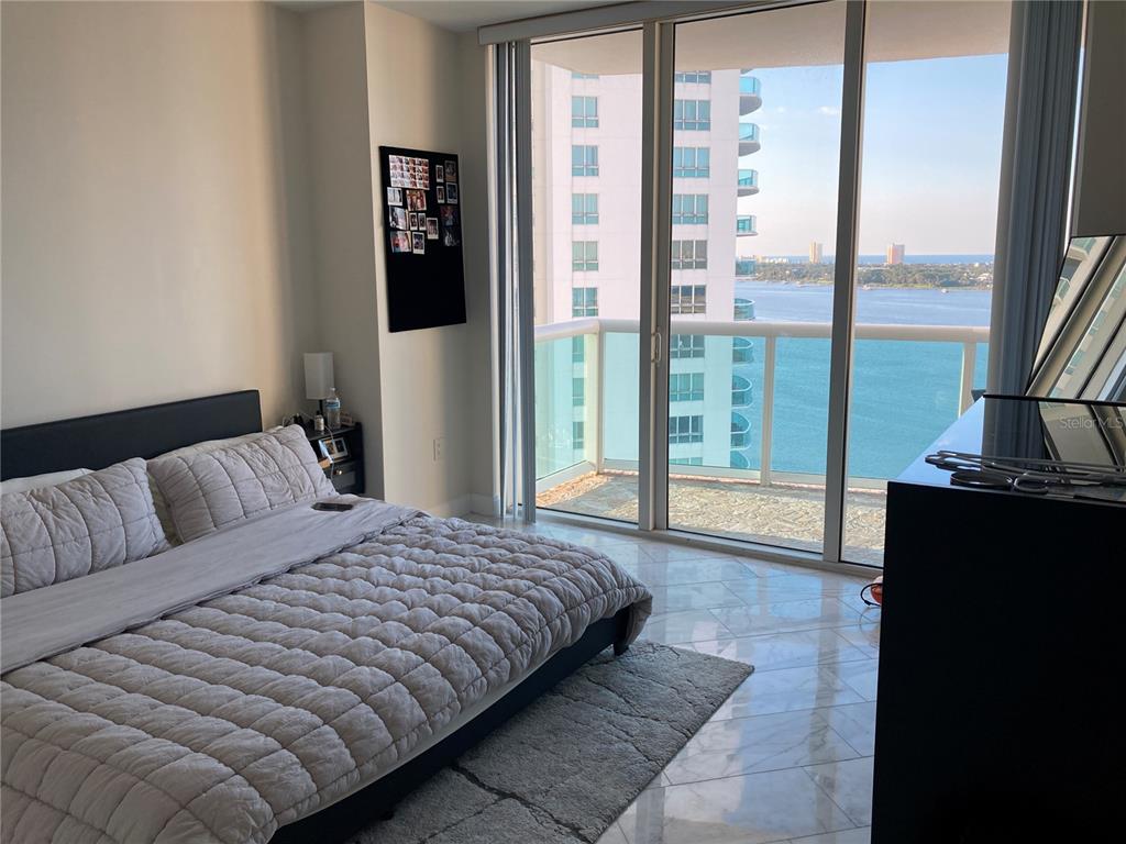 A bedroom features a bed, marble floors, and a balcony overlooking a bay and buildings — 231 RIVERSIDE DRIVE UNIT 1504-1, DAYTONA BEACH, FL