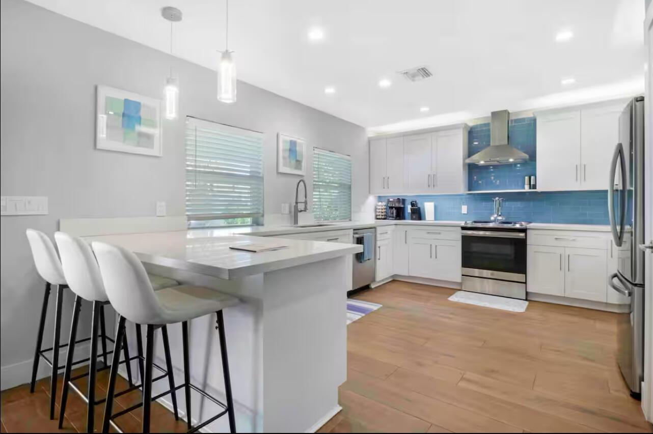 A modern kitchen features white cabinetry, a blue tile backsplash, and a breakfast bar island — 623 Jaeger Drive, Delray Beach FL 33444, DELRAY BEACH, FL