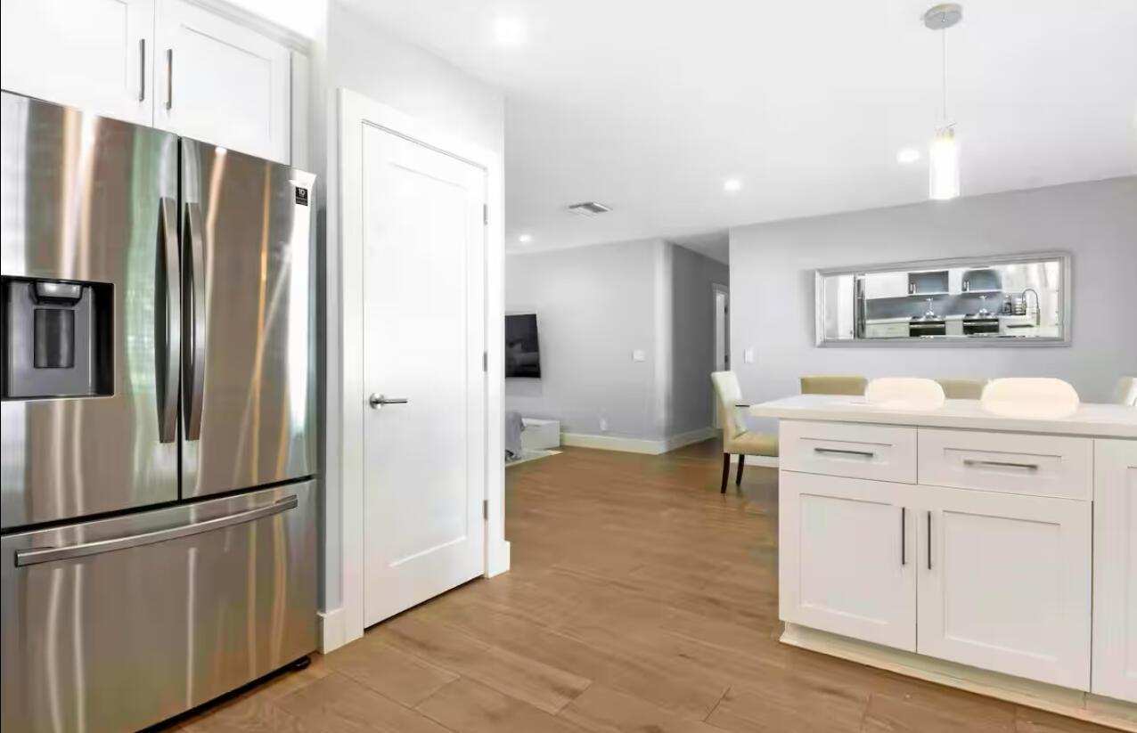 A modern kitchen features white cabinetry, stainless steel appliances, and light wood flooring — 623 Jaeger Drive, Delray Beach FL 33444, DELRAY BEACH, FL