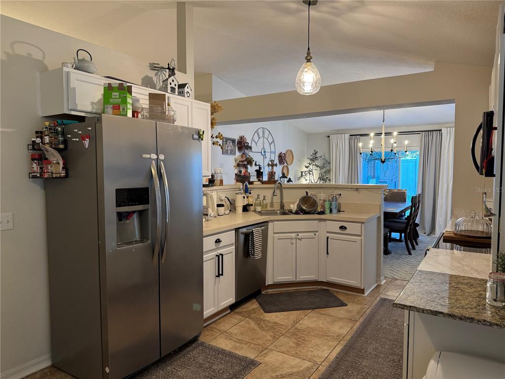 A kitchen with stainless steel appliances, white cabinets, and a view into the dining area — 439 HAMMERSTONE AVENUE, HAINES CITY, FL
