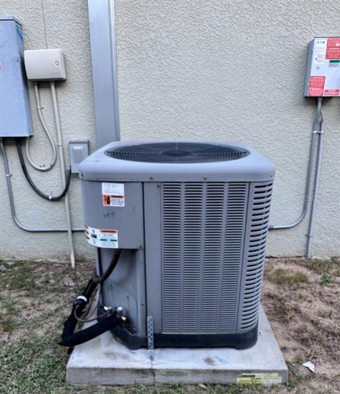 An outdoor air conditioning condenser unit sits on a concrete pad against a stucco wall — 439 HAMMERSTONE AVENUE, HAINES CITY, FL