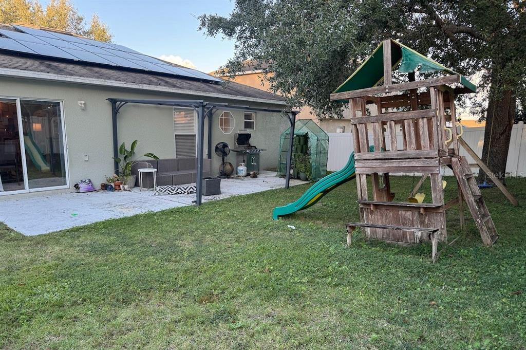 A backyard features a patio with a pergola, a grill, and a wooden playset — 439 HAMMERSTONE AVENUE, HAINES CITY, FL