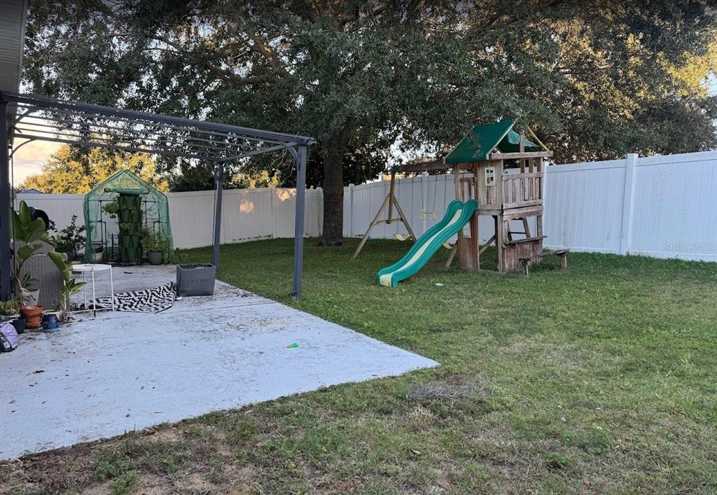 A backyard features a concrete patio with a pergola, a play set, and a greenhouse — 439 HAMMERSTONE AVENUE, HAINES CITY, FL