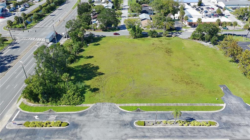An aerial view shows a vacant, grassy lot bordered by a paved road and parking area — 945 6TH STREET, DAYTONA BEACH, FL