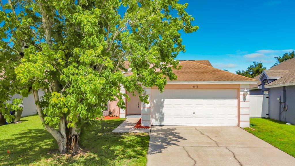 A single-story house with a two-car garage and a large tree in the front yard — 2079 SHANNON LAKES BOULEVARD, KISSIMMEE, FL
