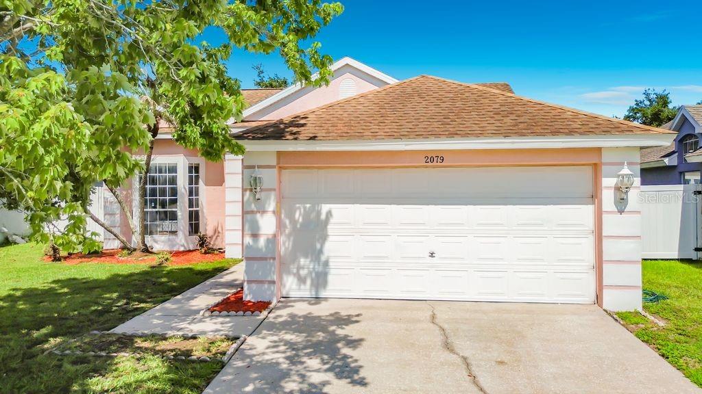 A single-story house with a white garage door, tan roof, and pink exterior walls — 2079 SHANNON LAKES BOULEVARD, KISSIMMEE, FL