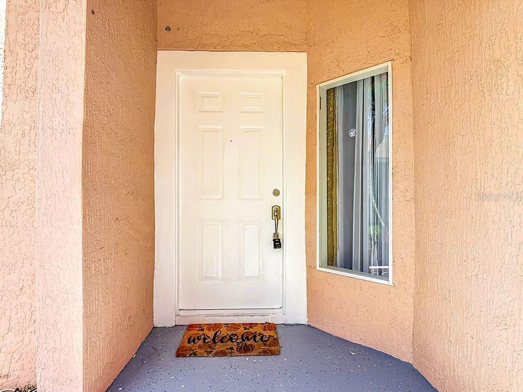 A white front door with a side window and a welcome mat on a porch — 2079 SHANNON LAKES BOULEVARD, KISSIMMEE, FL