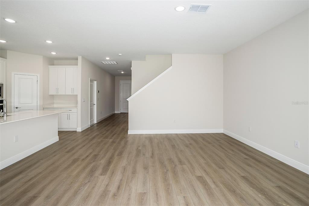 An open-concept living area features light wood-look flooring, white walls, and a kitchen island — 33577 TWILIGHT SEA PLACE, DADE CITY, FL