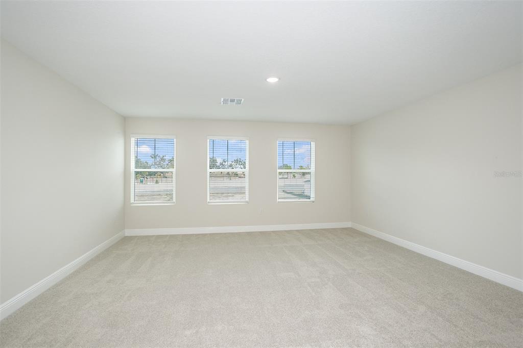 An empty room features beige walls, neutral carpeting, and three windows with white blinds — 33577 TWILIGHT SEA PLACE, DADE CITY, FL