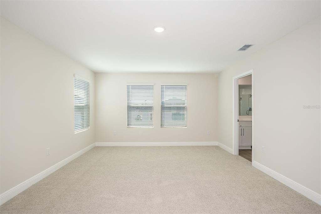 An empty bedroom with beige carpet, light-colored walls, three windows with blinds, and a doorway — 33577 TWILIGHT SEA PLACE, DADE CITY, FL