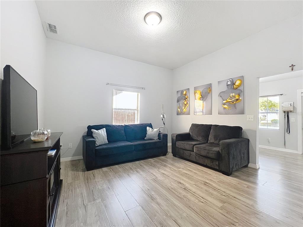 A living room features light wood-look flooring, two dark sofas, and three abstract wall art pieces — 1109 5TH STREET SW, WINTER HAVEN, FL