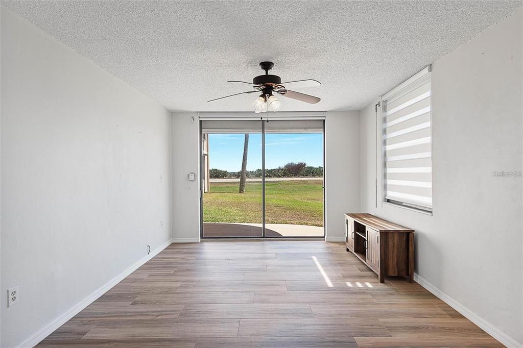 An empty living room features wood-look flooring, a ceiling fan, and sliding glass patio doors — 3360 OCEAN SHORE BOULEVARD UNIT 1030, ORMOND BEACH, FL