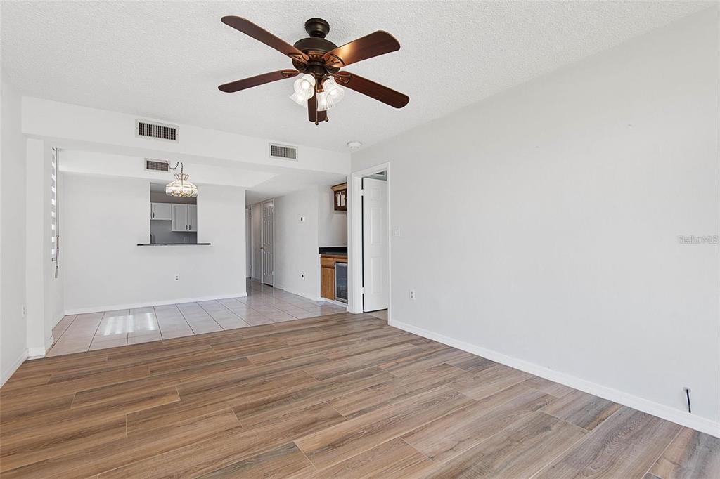 A living room with wood-look flooring leads to a tiled dining area and kitchen — 3360 OCEAN SHORE BOULEVARD UNIT 1030, ORMOND BEACH, FL