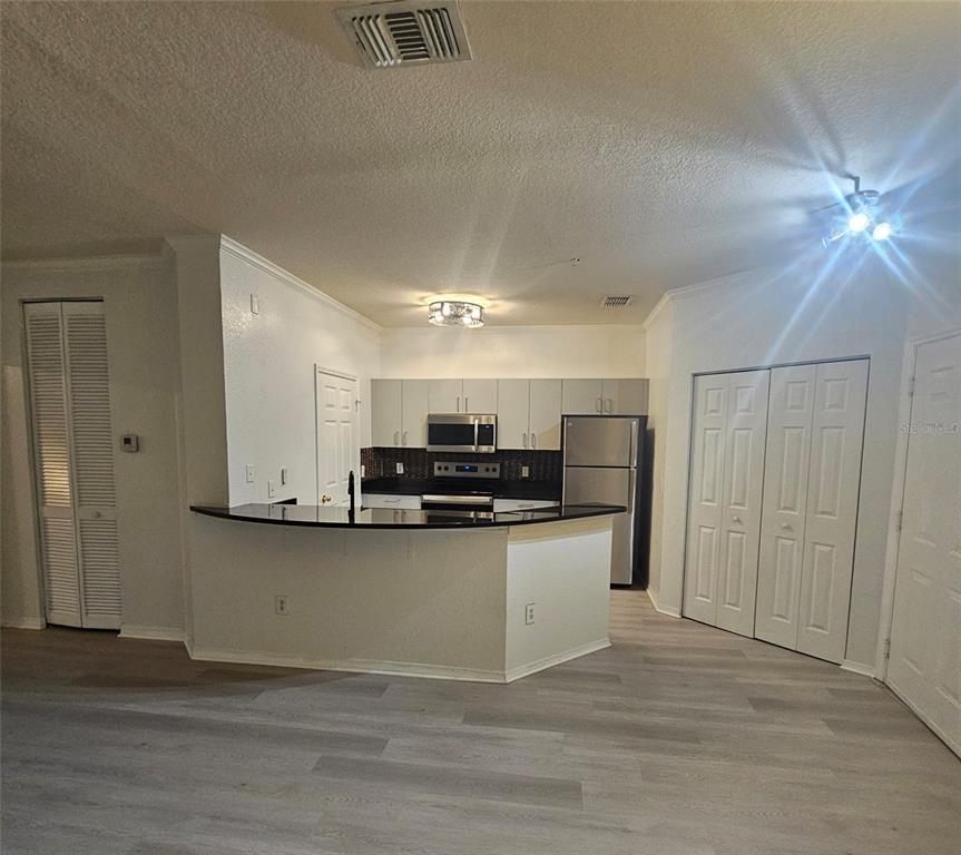 A kitchen with stainless steel appliances, dark countertops, and light-colored cabinets opens to a living area — 3621 CONROY ROAD UNIT 738, ORLANDO, FL