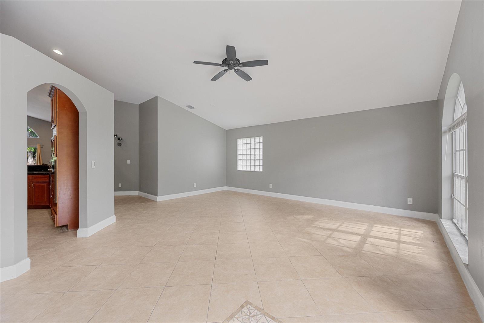 An empty living room features light tile floors, gray walls, a ceiling fan, and arched doorways — 1851 Oak Berry Circle, Wellington FL 33414, WELLINGTON, FL