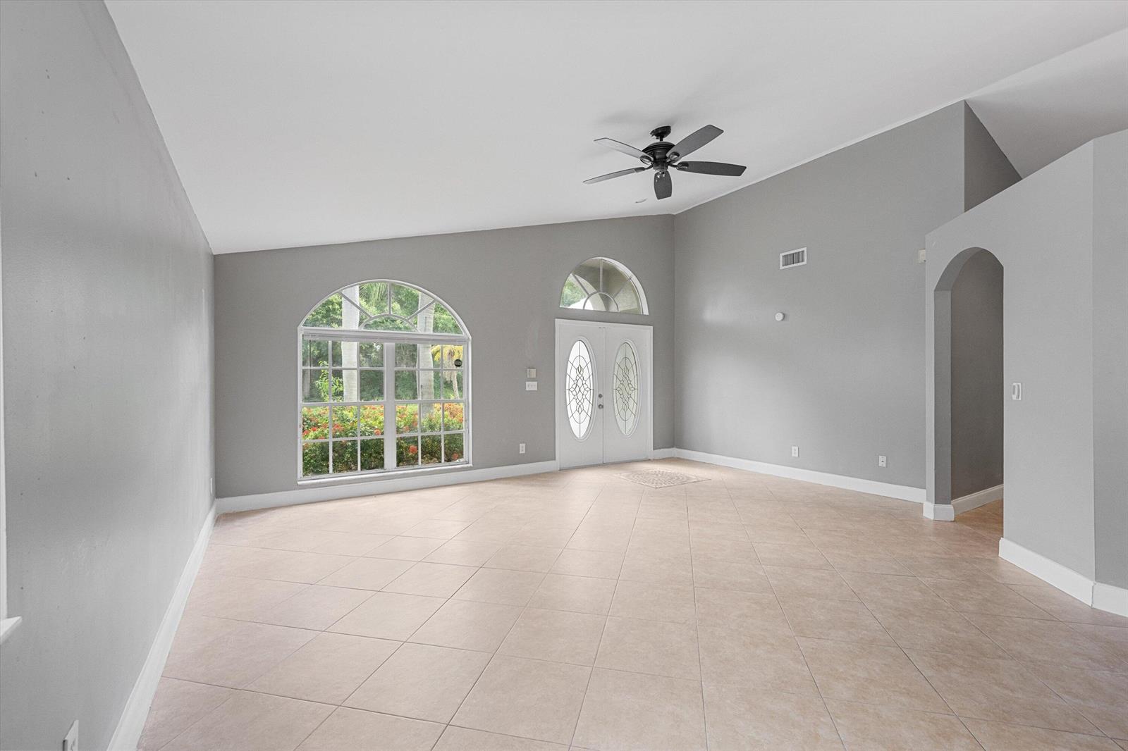 An empty living room features gray walls, tile flooring, a vaulted ceiling, and arched windows — 1851 Oak Berry Circle, Wellington FL 33414, WELLINGTON, FL