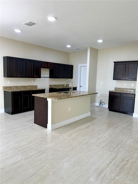 A kitchen features dark wood cabinets, granite countertops, a center island, and light-colored tile flooring — 4669 OSPREY WAY, WINTER HAVEN, FL