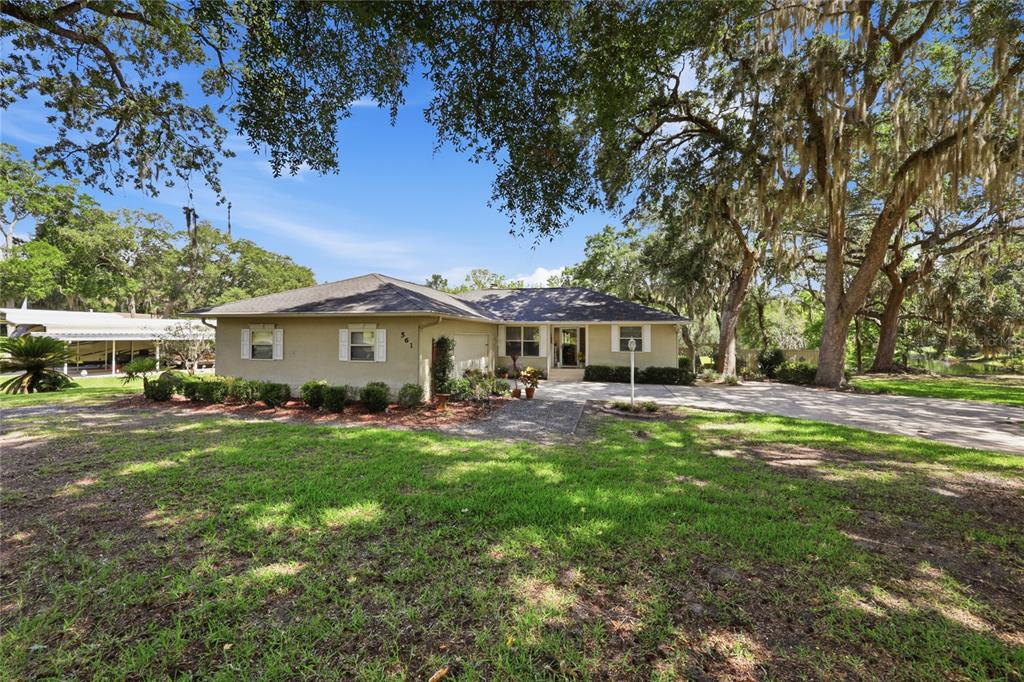 A single-story house with a tan exterior sits on a grassy lot under large trees — 561 SE 28TH STREET, MELROSE, FL
