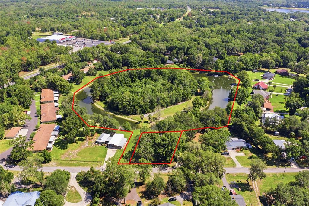 An aerial view shows a wooded lot surrounded by a pond with nearby residential buildings — 561 SE 28TH STREET, MELROSE, FL