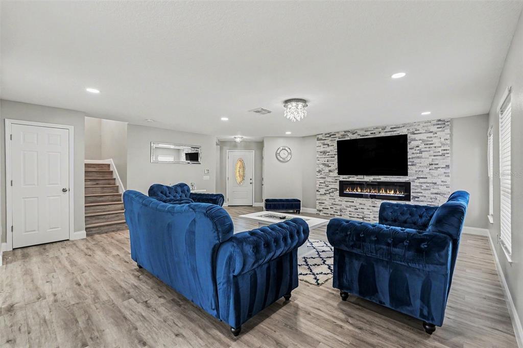A living room features blue tufted sofas, a stone fireplace wall, and wood-look flooring — 6222 CHERRY BLOSSOM TRAIL, GIBSONTON, FL