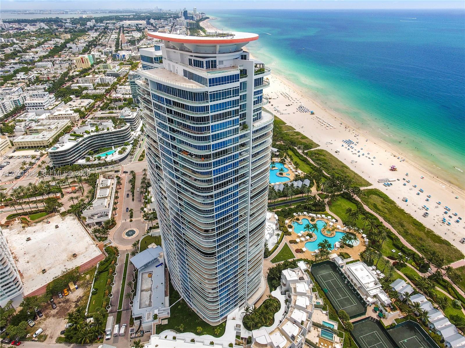 An aerial view shows a tall, modern residential skyscraper situated between a beach and city — 100 S Pointe Dr # 2806, Miami Beach FL 33139, MIAMI BEACH, FL