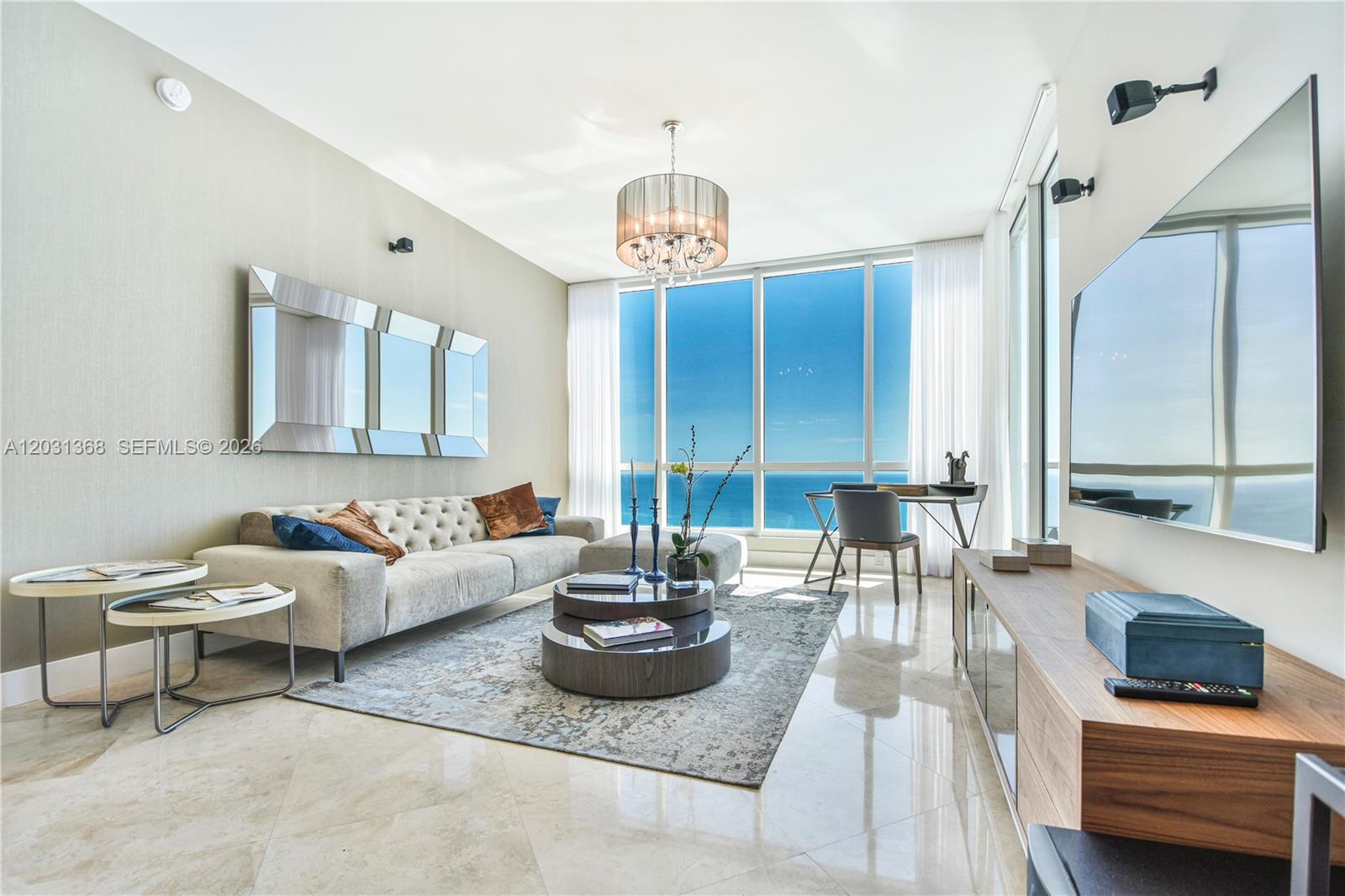 A modern living room features a tufted sofa, circular coffee tables, and floor-to-ceiling ocean views — 100 S Pointe Dr # 2806, Miami Beach FL 33139, MIAMI BEACH, FL