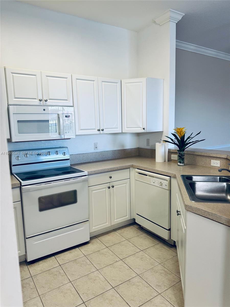 A kitchen features white cabinets, white appliances, tan countertops, and light-colored tile flooring — 4702 SW 160th Ave # 337, Miramar FL 33027, MIRAMAR, FL