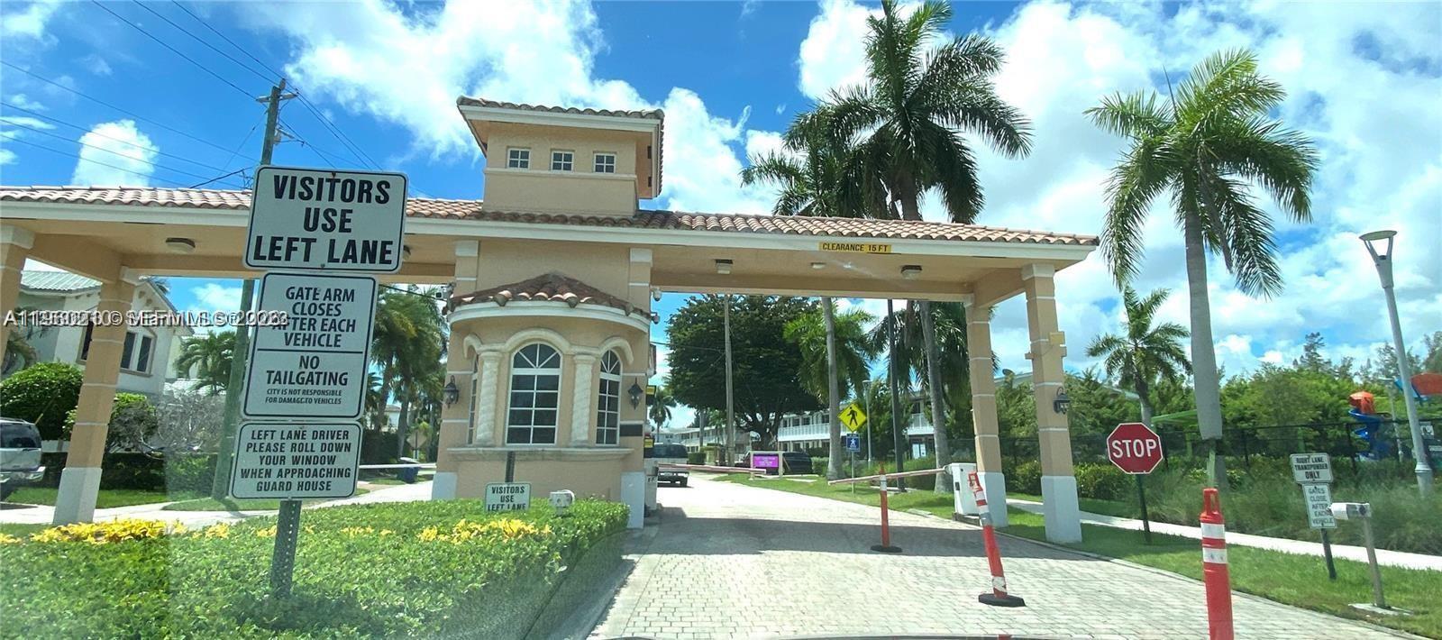 A gated community entrance features a guard house, palm trees, and traffic signage — 600 Layne # 216, Hallandale Beach FL 33009, HALLANDALE BEACH, FL