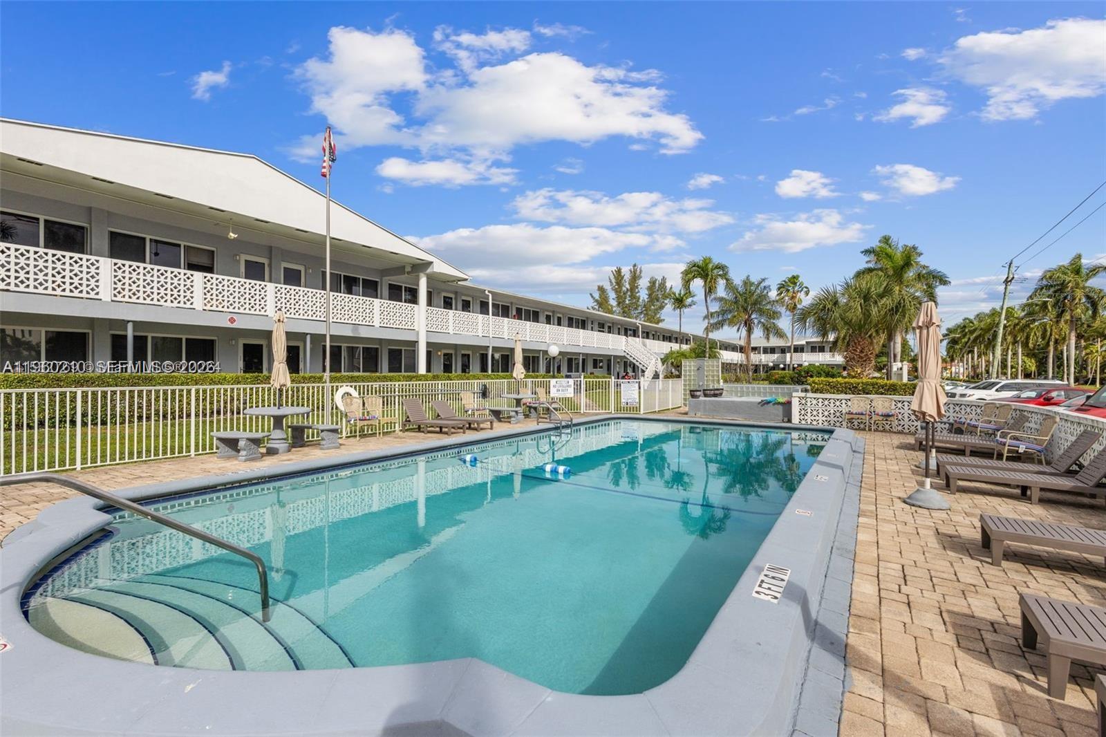 A rectangular swimming pool sits on a paved deck in front of a multi-story building — 600 Layne # 216, Hallandale Beach FL 33009, HALLANDALE BEACH, FL