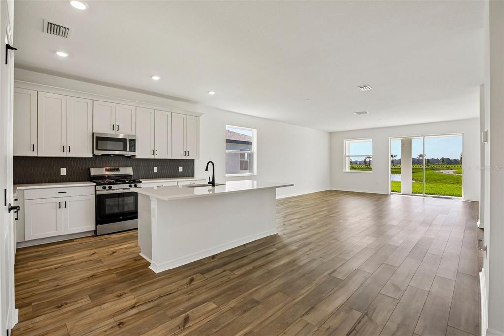 A modern kitchen with white cabinets and an island opens into a spacious living area — 13810 BERTRAND AVENUE, PALMETTO, FL