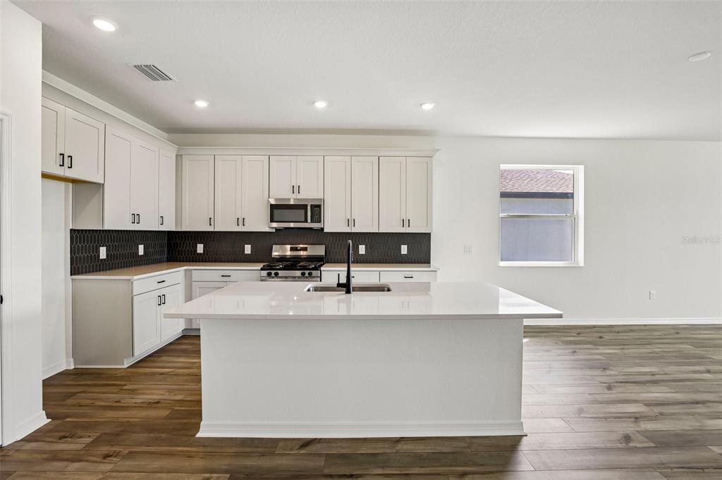 A modern kitchen features white cabinets, a large central island, and dark tile backsplash — 13810 BERTRAND AVENUE, PALMETTO, FL
