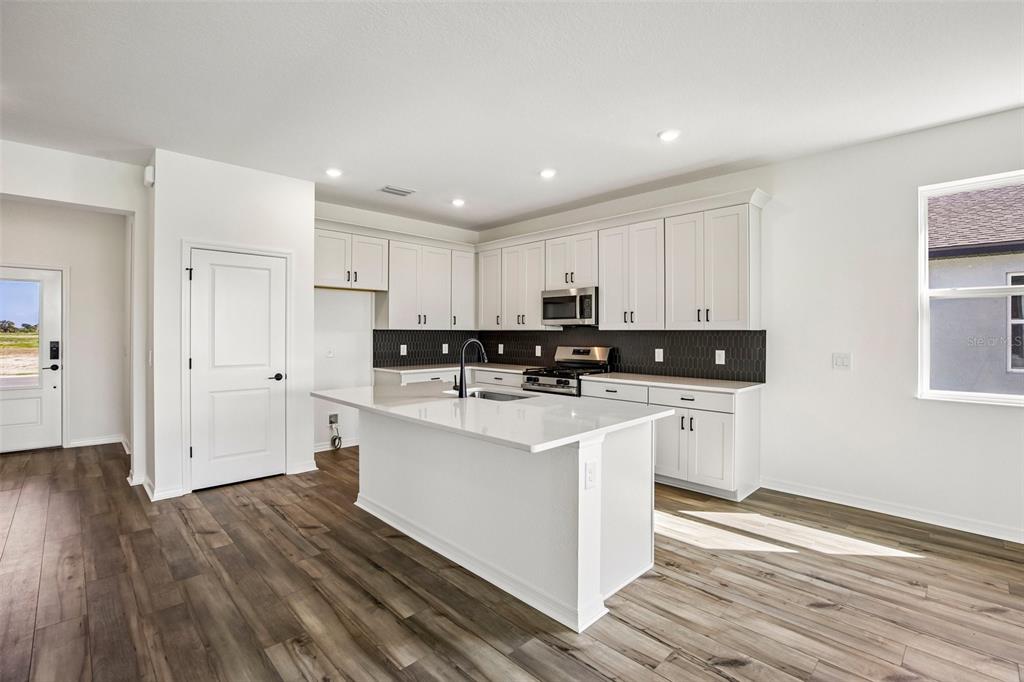 A modern kitchen features white cabinetry, a central island, and dark tile backsplash — 13810 BERTRAND AVENUE, PALMETTO, FL