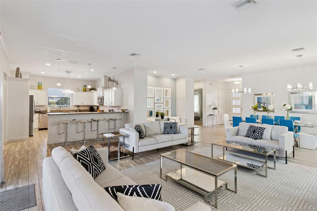 An open-concept living room and kitchen feature light tile floors, white cabinetry, and modern furniture — 7423 SPARKLING COURT, REUNION, FL