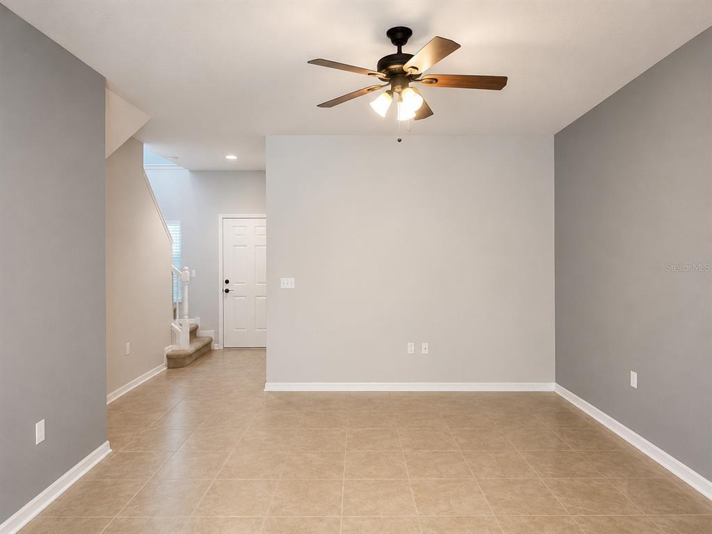 An empty room with tiled floors, a ceiling fan, and a staircase in the background — 5602 RUTHERFORD PLACE, OVIEDO, FL