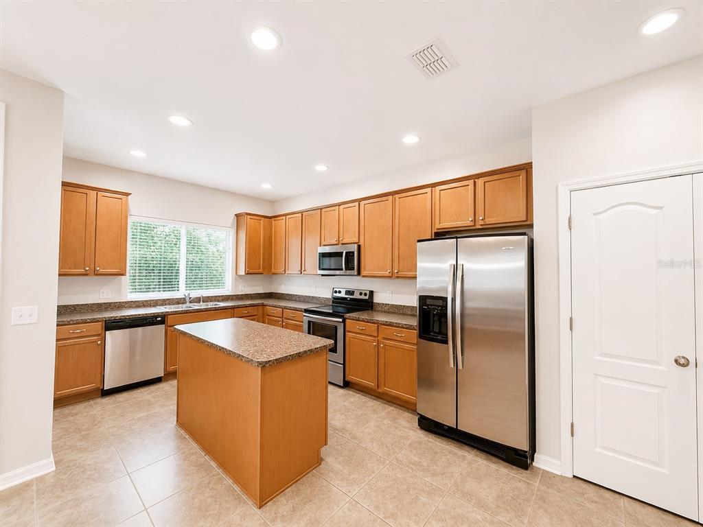 A kitchen features light wood cabinets, granite countertops, stainless steel appliances, and a central island — 5602 RUTHERFORD PLACE, OVIEDO, FL