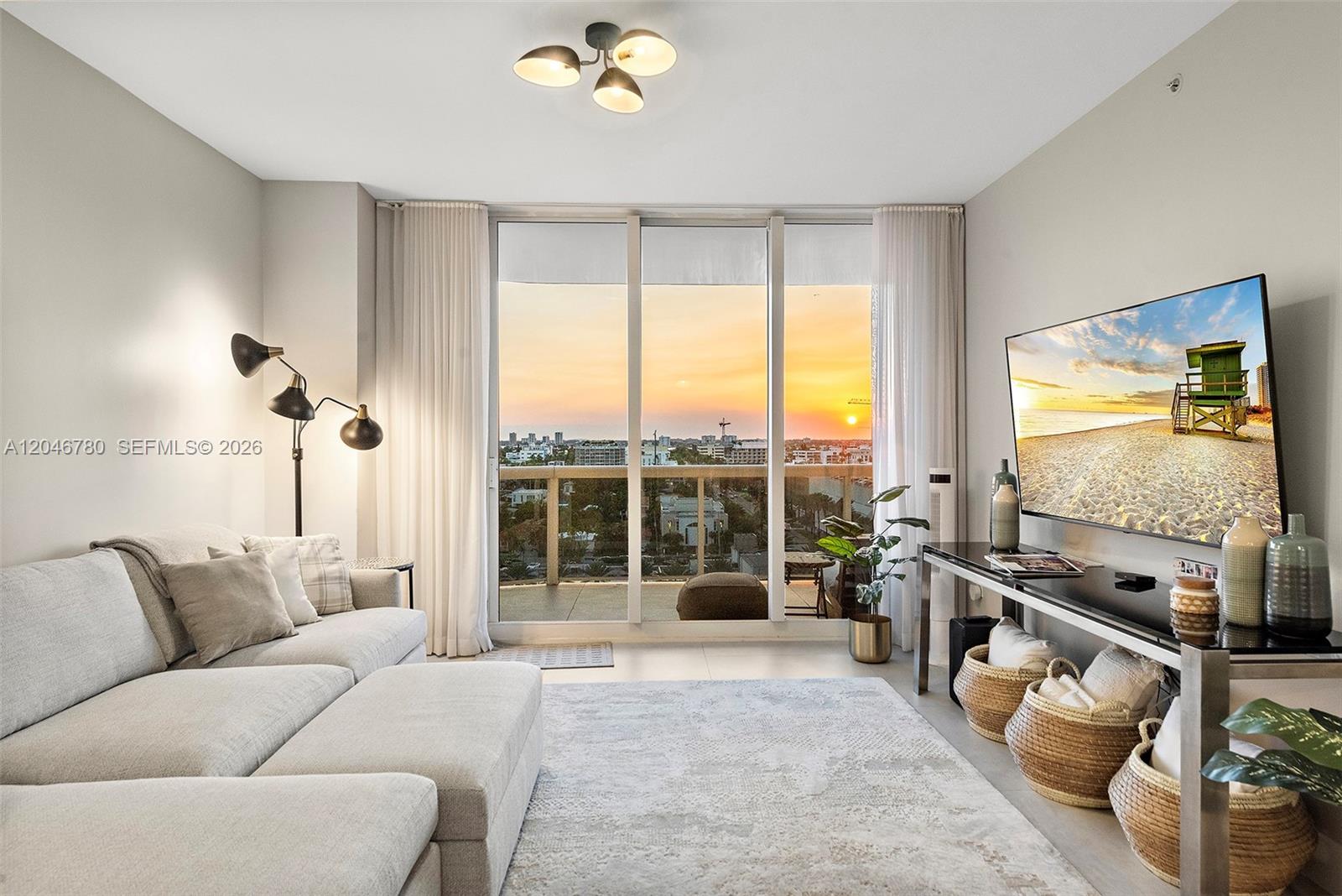 A living room features a sectional sofa, a television, and floor-to-ceiling windows overlooking a sunset — 9595 Collins Ave, Surfside FL 33154, SURFSIDE, FL