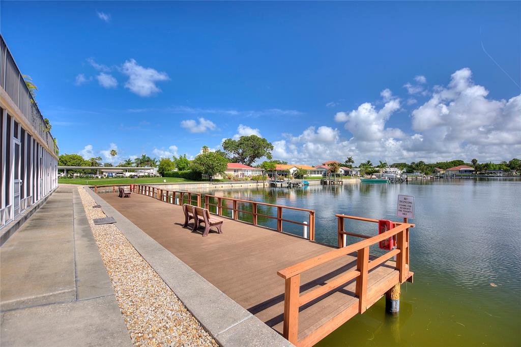 A wooden dock with benches extends into a canal lined with houses and palm trees — 3753 46TH AVENUE S UNIT 10, ST PETERSBURG, FL