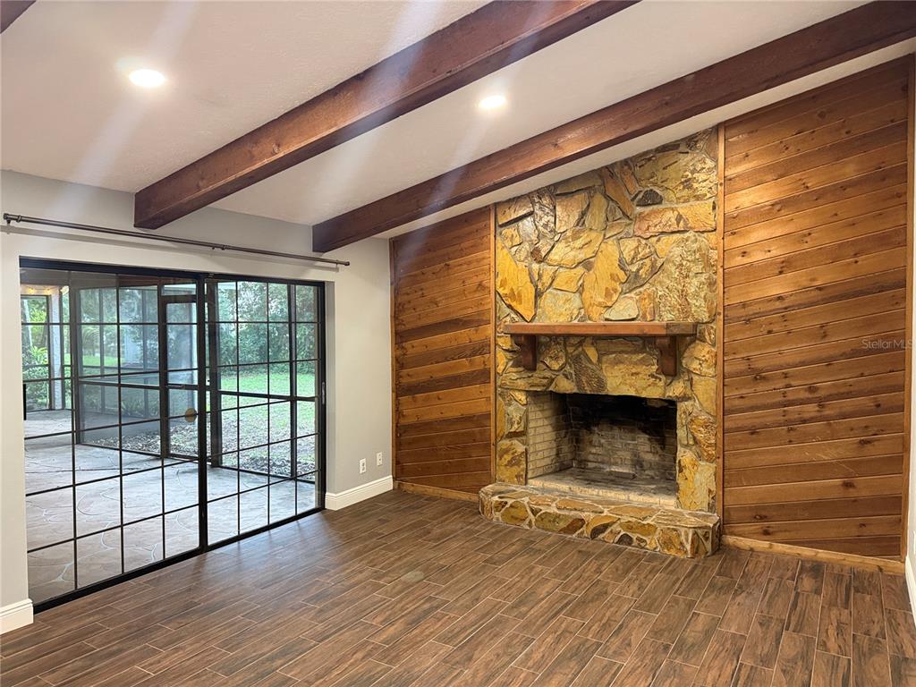 A living room features wood-look tile flooring, exposed ceiling beams, and a stone fireplace wall — 9217 KINGSRIDGE DRIVE, TEMPLE TERRACE, FL