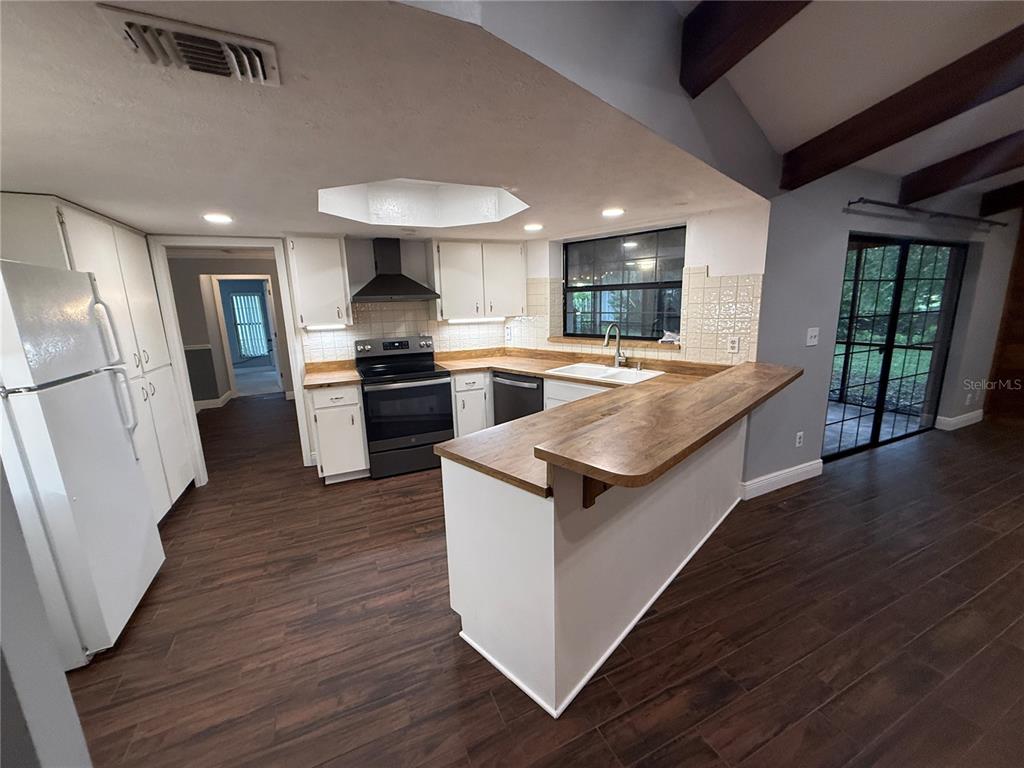 A kitchen with white cabinets and wood countertops overlooks a living area with exposed beams — 9217 KINGSRIDGE DRIVE, TEMPLE TERRACE, FL