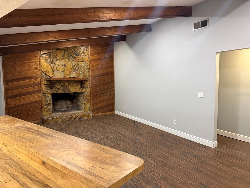 A living area with wood-look tile floors, exposed ceiling beams, and an open kitchen — 9217 KINGSRIDGE DRIVE, TEMPLE TERRACE, FL