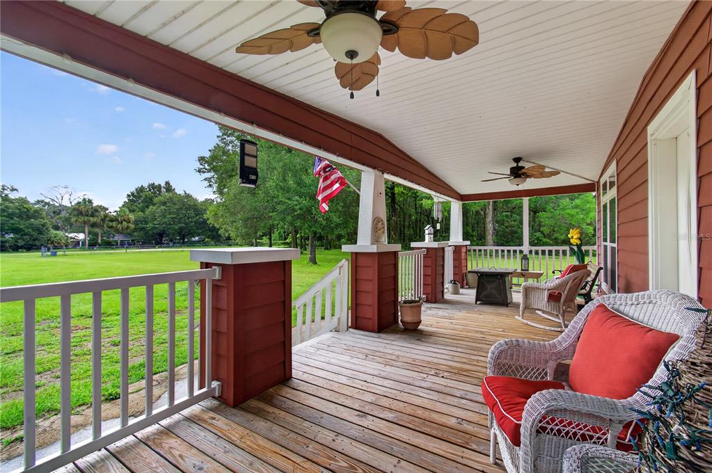 A covered wooden porch features white railings, ceiling fans, and wicker furniture overlooking a lawn — 17860 NW 73RD TERRACE, TRENTON, FL