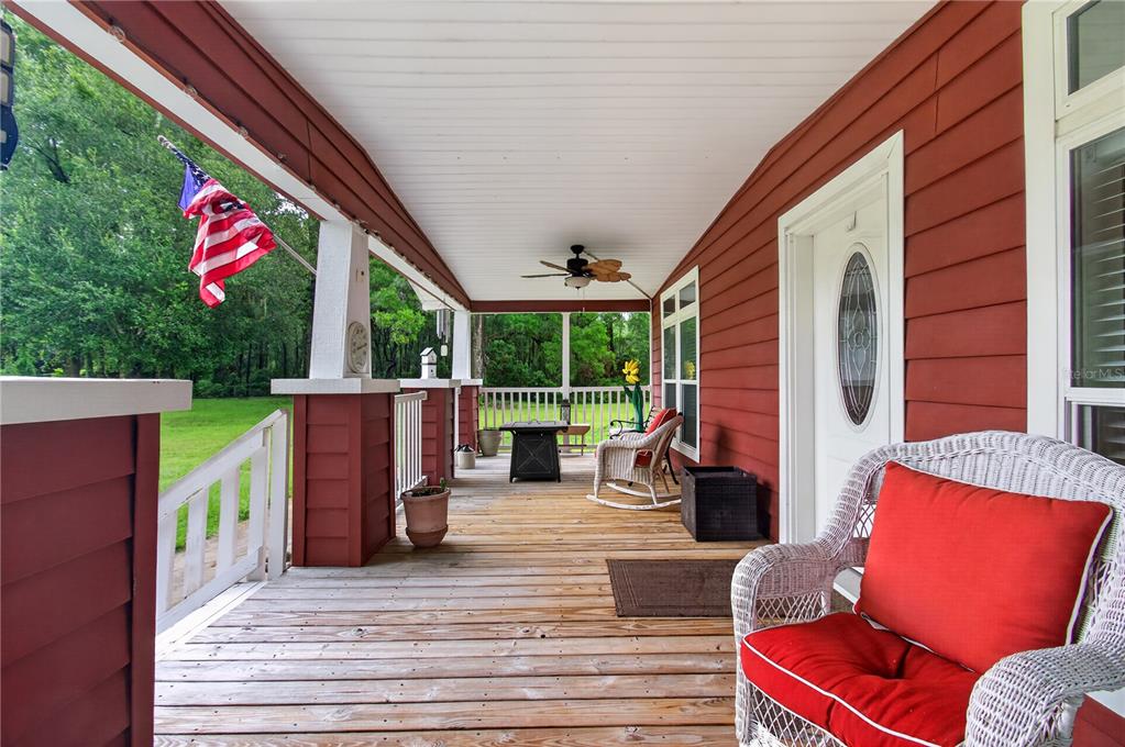 A covered wooden porch features red siding, white railings, and outdoor seating — 17860 NW 73RD TERRACE, TRENTON, FL