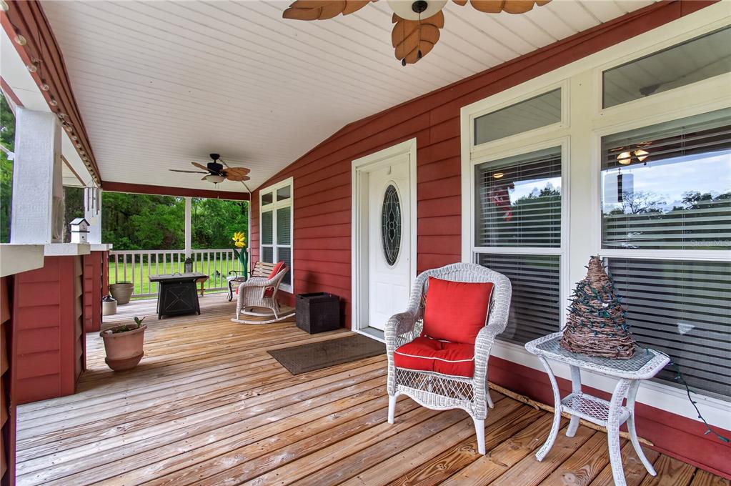 A covered wooden porch features red siding, white trim, wicker chairs, and a ceiling fan — 17860 NW 73RD TERRACE, TRENTON, FL