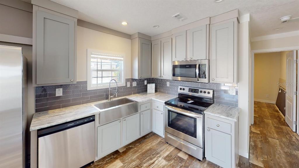 A kitchen features light gray cabinets, stainless steel appliances, a farmhouse sink, and tile backsplash — 1556 BLUE HERON DRIVE, ENGLEWOOD, FL