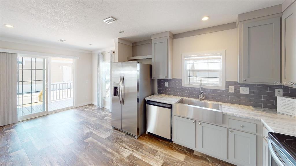 A kitchen features gray cabinets, stainless steel appliances, a farmhouse sink, and wood-look flooring — 1556 BLUE HERON DRIVE, ENGLEWOOD, FL