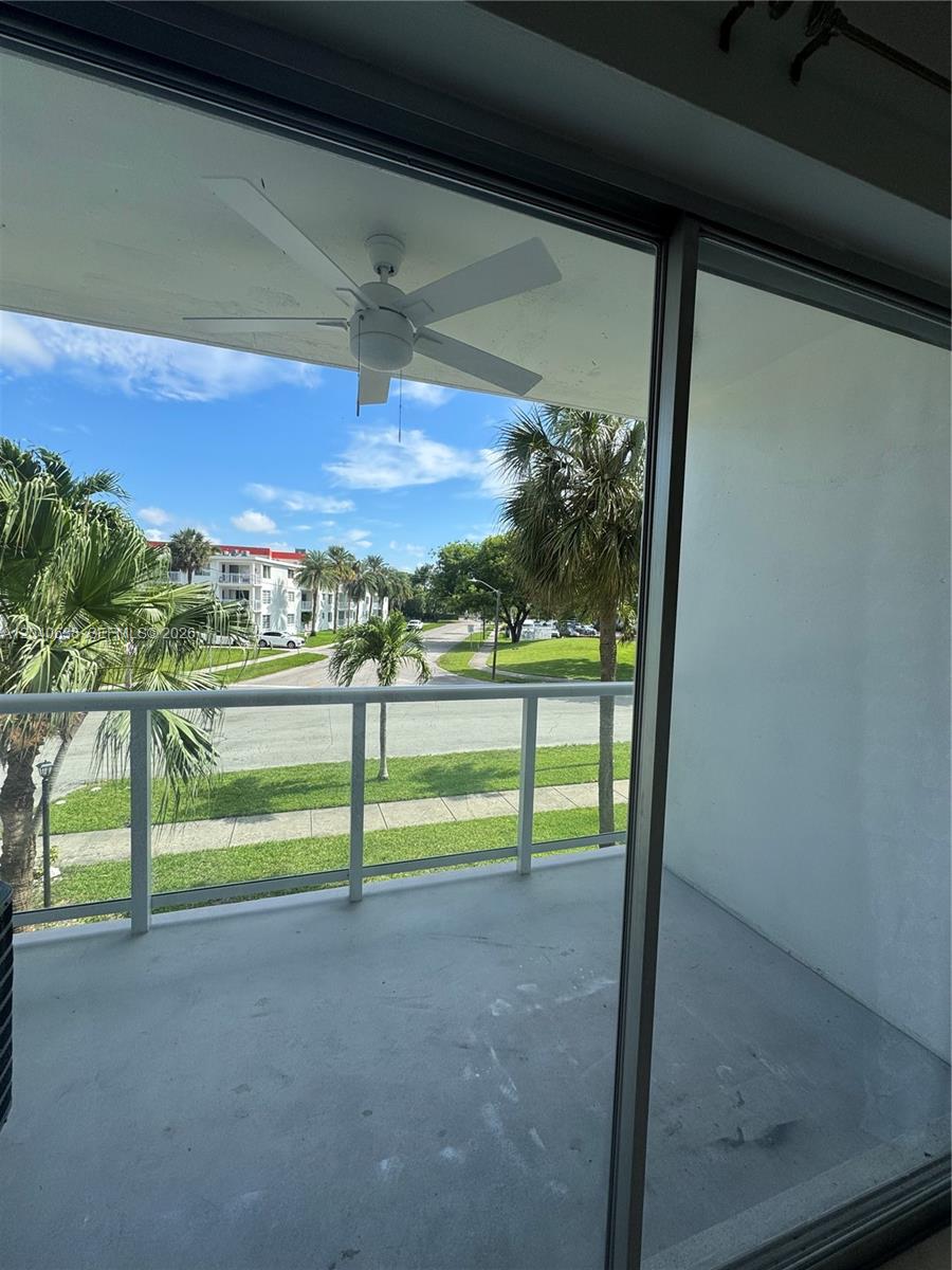 A balcony with a white ceiling fan overlooks a street, palm trees, and apartment buildings — 1600 NE 114th St # 204, Miami FL 33181, MIAMI, FL