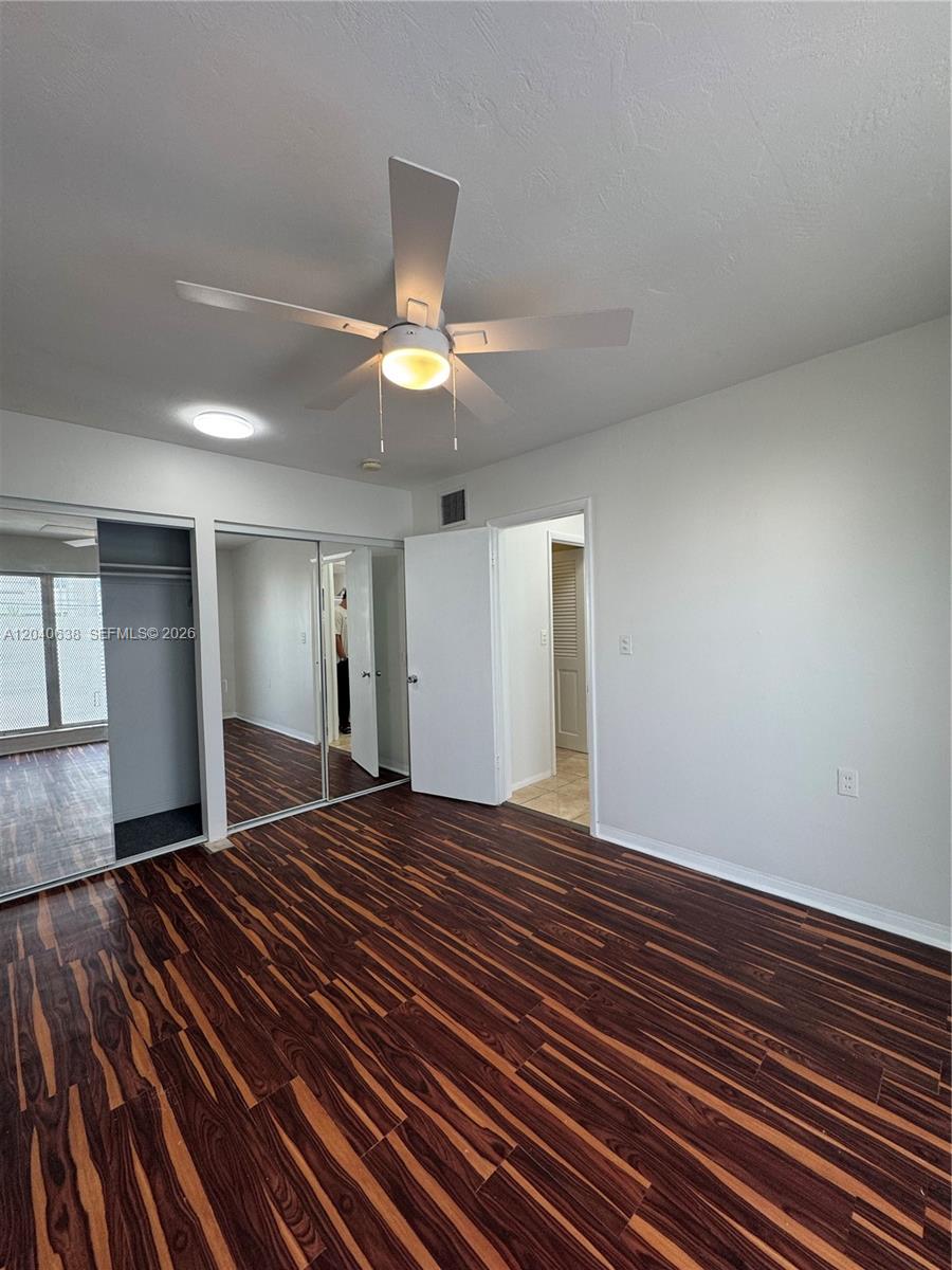 A bedroom features dark wood-look flooring, a ceiling fan, and mirrored closet doors — 1600 NE 114th St # 204, Miami FL 33181, MIAMI, FL