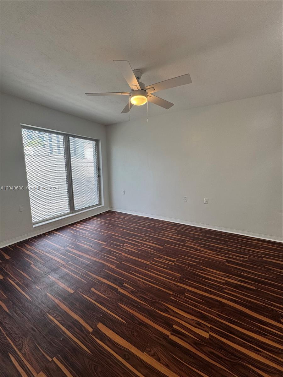 An empty room features dark wood-look flooring, white walls, and a ceiling fan — 1600 NE 114th St # 204, Miami FL 33181, MIAMI, FL