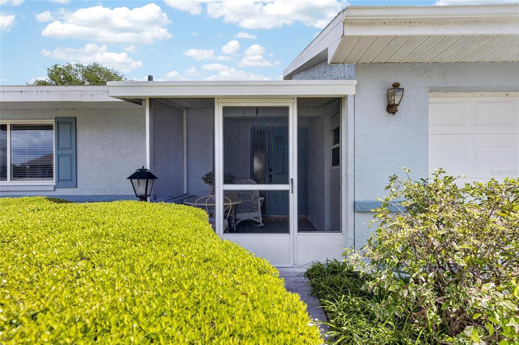 A light blue house exterior features a screened-in front porch, a hedge, and a garage — 1517 INGRAM DRIVE, SUN CITY CENTER, FL
