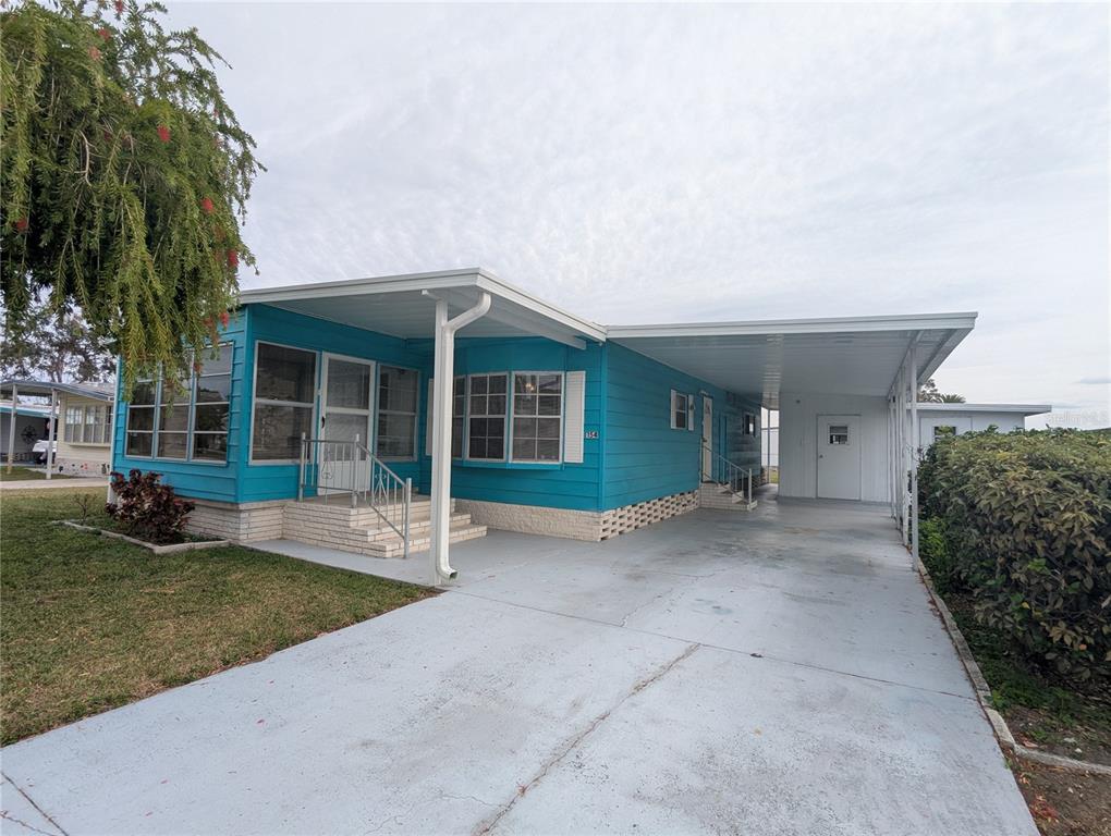 A bright blue mobile home features a concrete driveway, a carport, and a front porch — 1610 REYNOLDS ROAD UNIT 154, LAKELAND, FL